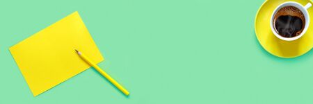 A cup of hot tasty coffee and sheet of yellow paper for notes on green table in the home office. ...
