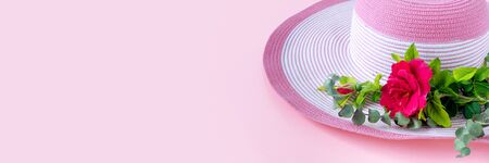 Beautiful straw hat with bouquet of roses and eucalyptus on sunny day. Nature pink paper background. 

Creative greeting card.の写真素材