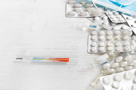 Pills and thermometer on white wooden background. Flat lay, top view, copy space concept.