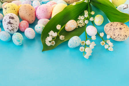 Beautiful Easter card with colorful eggs and delicate lilies of the valley on paper blue background. Flat lay, top view, copy space concept. Copyspace for your textの写真素材