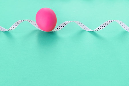 Beautiful easter card with pink painted egg and white ribbon on paper green background.の写真素材