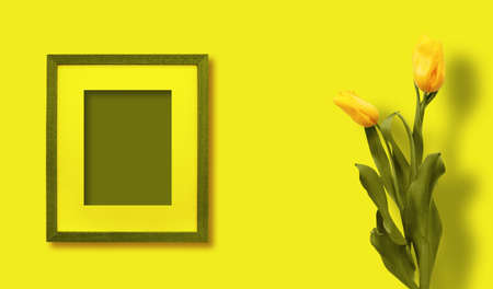 Beautiful yellow tulips with green foliage in vintage wooden frame on bright green wall for holiday....