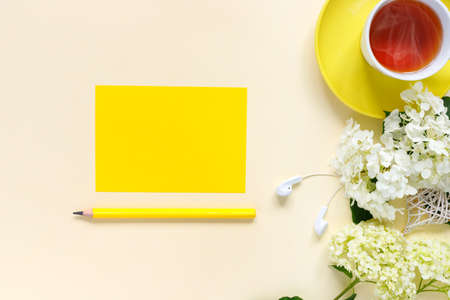 Top view of home office desk with with notepad, pencil, cup of hot tea, and bouquet of hydrangeas on yellow paper background. Flat lay, top view, copy space concept.の写真素材