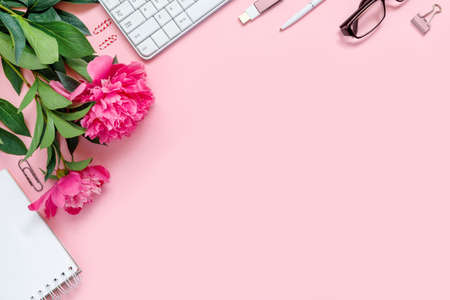Laptop, accessories and bouquet of beautiful peonies with glasses and headphones on pink background. Flat lay of working place. Top view concept, copy space frame for text.の写真素材