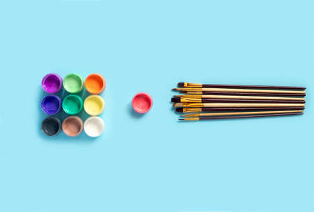 Paints and brushes for painting on blue paper background. Flat lay, top view, copy space concept.