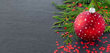Red Christmas toy balls, holiday confetti and christmas tree branches on black background. New...