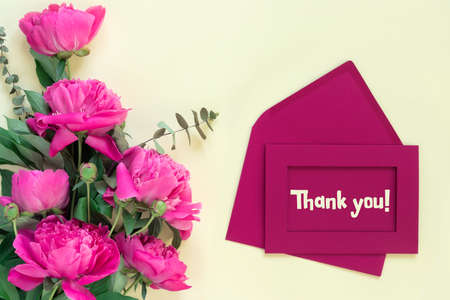 Beautiful delicate pink peonies with envelope and letter on yellow paper background. Thank you lettering on the card. Creative design. Appreciation for the service. Inscription in English.の写真素材