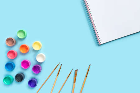 Paints, brushes and album for painting on blue paper background. Flat lay, top view, copy space...