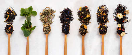 Large assortment of dry tea in spoons from herbs, flowers, berries and fruits on on stone marble...