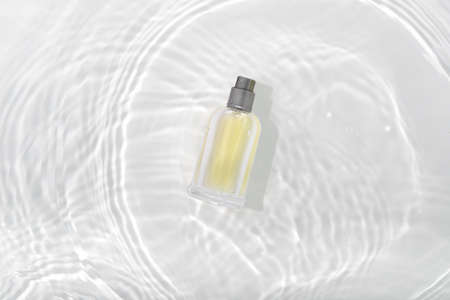 Cosmetics perfume bottle on splashing water surface with circles on white background. Glass spray tube package promo mockup banner design. Flat lay, top view, copy space concept.の写真素材
