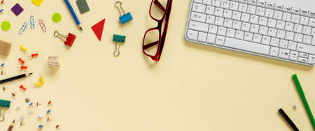 School and office supplies border with keyboard on beige paper background. Multicolored pencils,...