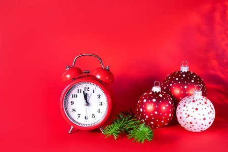Red and white Christmas balls, alarm clock and tree branches on red paper background. 5 minutes before the New Year. Minimal celebration concept with copy space.の写真素材