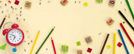 School and office supplies border with red alarm clock on beige paper background. Multicolored pencils, paints, plasticine, abacus, pushpins and other school accessories Flat lay top view with copy space. Back to school concept.の写真素材
