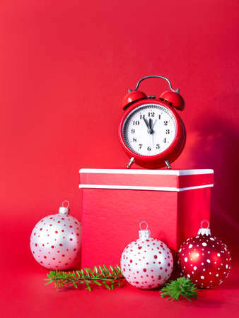Alarm clock with colorful Christmas balls, tree branches and red gift boxes on paper background. 5 minutes before the New Year. Creative greeting card. Minimal celebration concept with copy space.の写真素材