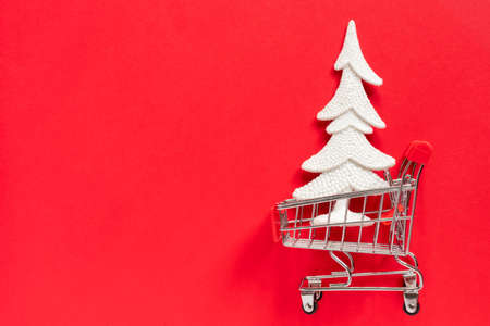 Grocery shopping cart with gift box and New Year tree on red background. Minimal celebration concept with copy space. Flat lay, top view.の写真素材