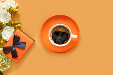 Gift box with white hydrangea and rose flowers on orange background. Cup of hot coffee. Conceptual postcard for the holiday. Flat lay, top view concept with copy space for text.の写真素材