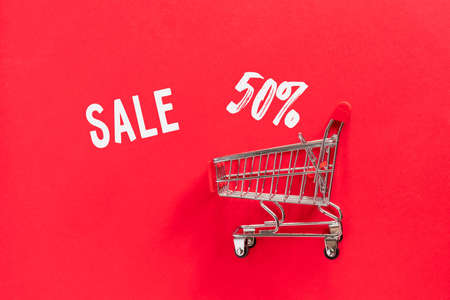 Grocery shopping cart with gift box on red background. Minimal celebration concept with copy space. Flat lay, top view.の写真素材