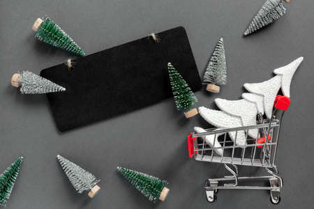Grocery shopping cart with gift box and New Year tree on black background. Minimal celebration concept with copy space. Flat lay, top view.の写真素材
