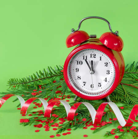 Alarm clock confetti, and tree branches on green paper background. 5 minutes before the New Year....