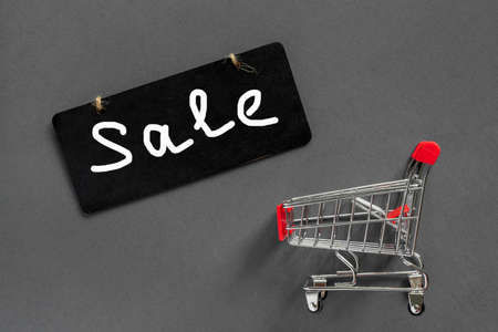 Grocery shopping cart with gift box on black background. Minimal celebration concept with copy space. Flat lay, top view with text Sale.の写真素材