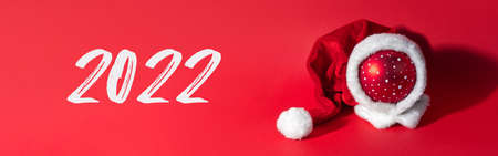 Multicolored Christmas ball in a hat of santa claus on a red background. The symbol of the new year and christmas. Creative greeting card copy space for text and date 2022 ..の写真素材