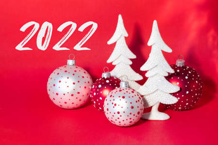Christmas card with snow-covered white New Year trees and colorful balls on bright red background....