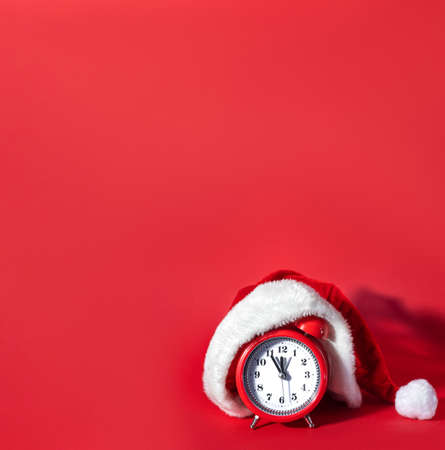 Red clock with Christmas Santa hat. Time for Christmas shopping concept. Blank copy space for text. New Years celebration creative.の写真素材