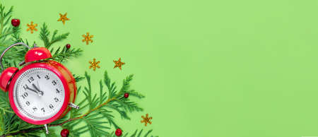 Alarm clock with tree branches on green paper background. 5 minutes before the New Year. Creative...