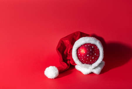 Multicolored Christmas ball in a hat of santa claus on a red background. The symbol of the new year and christmas. Creative greeting card copy space for text.の写真素材