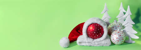 Red ball in hat of santa claus with white spruce tree on green background. The symbol of new year and christmas. Creative greeting card copy space for text.の写真素材