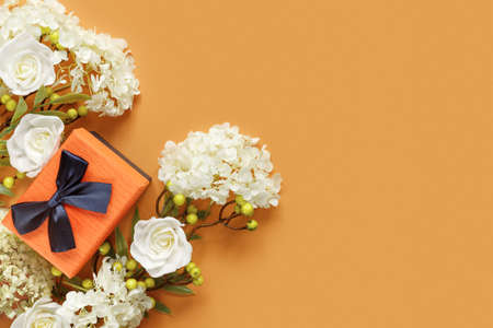 Gift box with white hydrangea and rose flowers on orange paper background. Conceptual postcard for holidays. Flat lay, top view concept with copy space for text.の写真素材