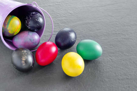Lots of bird bucket with painted Easter eggs on a dark tabletop. Holiday greeting card. Concept creative banner Flat lay top view with copy space.の写真素材