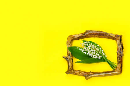Greeting card for mother's day with bouquet of tender lilies of the valley with wooden frame on yellow background. spring nature concept.の写真素材