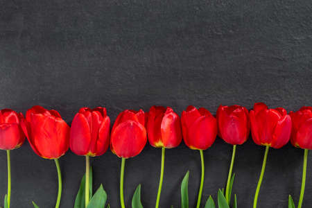 Bouquet of beautiful red tulips on black granite monument with empty space for text. Flat lay creative mockup.の写真素材
