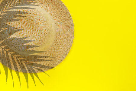 Fashionable straw hat with palm leaves on yellow paper background Flat lay, top view, copy space...