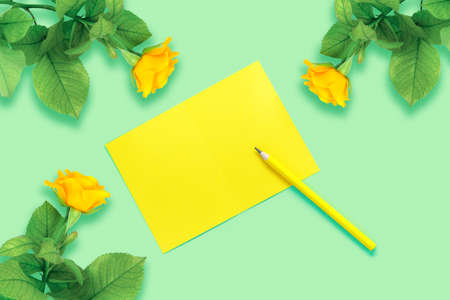 Beautiful bouquet of yellow roses and flower petals on a green table. Notebook and pencil for your text. Flat lay, top view, copy space concept.の写真素材