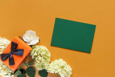 Gift box with white hydrangea and rose flowers on orange paper background. Conceptual postcard for holidays. Flat lay, top view concept with copy space for text.の写真素材