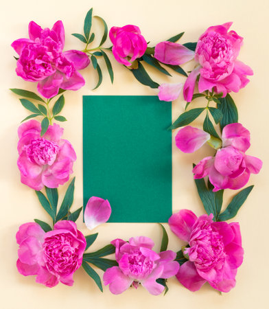 Garland of beautiful pink peonies on yellow paper background with postcard for congratulations or invitations. Creative floral wreath. Greeting card for holiday. Flat lay, top view concept with copy space for text.の写真素材
