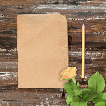 Pencil and sheet of brown paper with a yellow rose for text on wooden background. Flat lay, top view, copy space concept.の写真素材