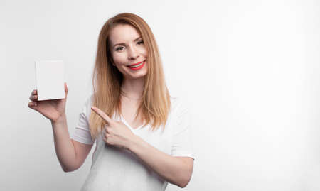 Person showing business card. Casual woman smiling holding the card. Shallow depth of field, focus on paper with empty copy space.の写真素材