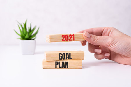 Businessman hand holding wooden cube with text 2021 GOAL, PLAN and ACTION on table background. Resolution, strategy, solution, goal, business and New Year holiday conceptsの写真素材