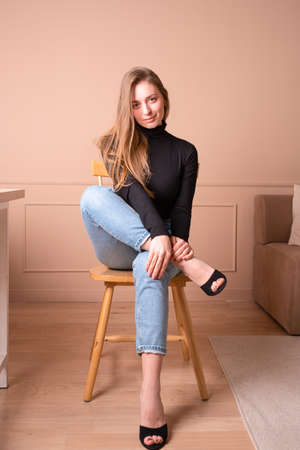 Full length portrait of a young serious woman in hat sitting on chair on the background.の写真素材