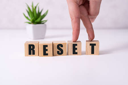 The hand puts a wooden cube with the letter R from the word Reset. The word is written on wooden cubes standing on the yellow surface of the tableの写真素材