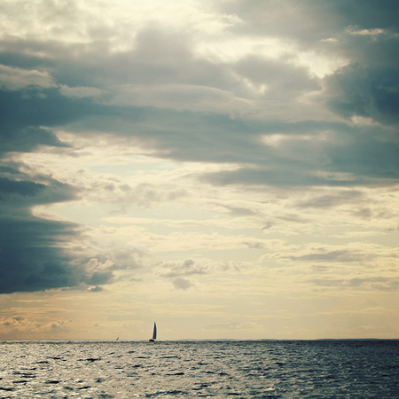Lake Ladoga with a boat on the horizon. Toned photo in vintage style. Sailing ship profile. Toned image. Rainy clouds. Calm water with a Sailing Vessel. Island of Valaam, Karelia, Russia.の写真素材