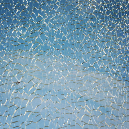 Blue sky behind broken glass surface. Abstract background. Aged photo. Hardened glass surface cracked on a small pieces. Cracked Texture.の写真素材