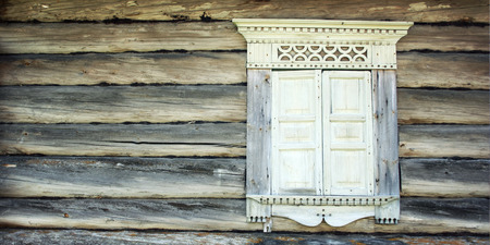 Closed window in abandoned house. Wooden frame with architraves and shutters. Facade of an old log cabin. Journey to the north of Russia. Kenozersky National Park (UNESCO Biosphere Reserve).の写真素材