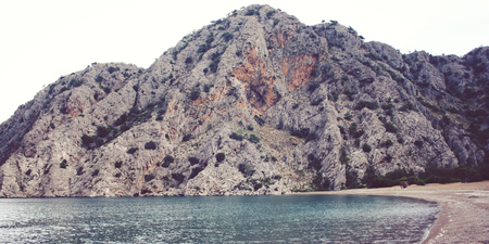 Rock covered with green bushes. View of Mediterranean sea bay. Southern coast of Turkey. Calm sea and cloudy sky. Spring day in Antalya province, Turkey.の写真素材