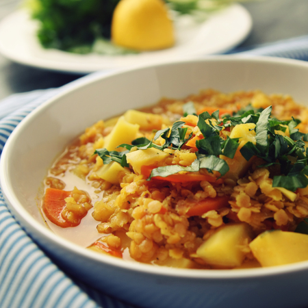 Red lentil stew on the round white plate. Vegetarian dish with potato, carrot and turmeric. European cuisine. Colorful vegan lunch. Selective focus.の写真素材