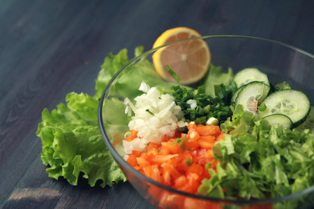 Glass bowl with cutted vegetables for a salad. Close up. Bell pepper, onion, leafy greens and tomatos cutted in peaces. Wooden background.の写真素材