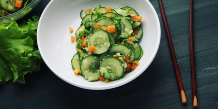 Chinese cucumber salad on the white plate. Top view. Chopsticks. Asian cuisine. Bell pepper, cucumber and sesame seeds. Wide photo. Vegetarian dish. Wide photo.の写真素材